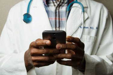 A doctor looking at their phone with both hands holding it.