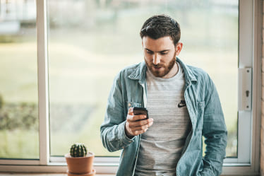 A man holding his phone by a window.