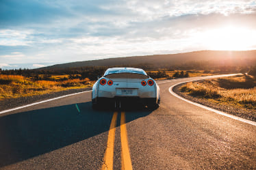 Car driving down a road in the sunset.