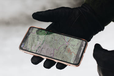 A gloved hand holding a phone in the snow.